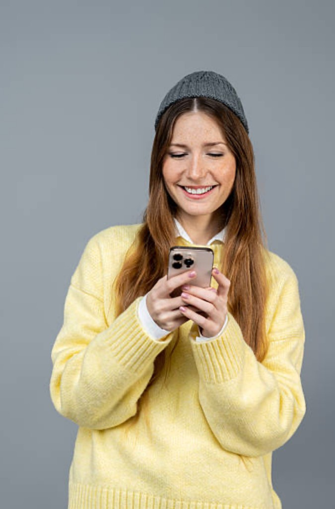 Smiling woman holding a smartphone against a grey background.